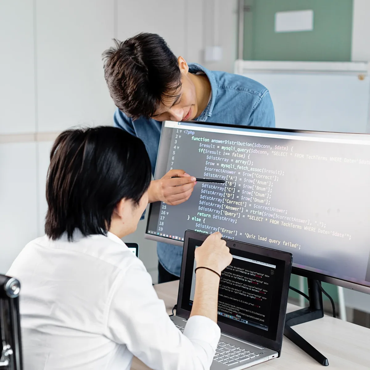 Two technology colleagues examining code on desktop monitors