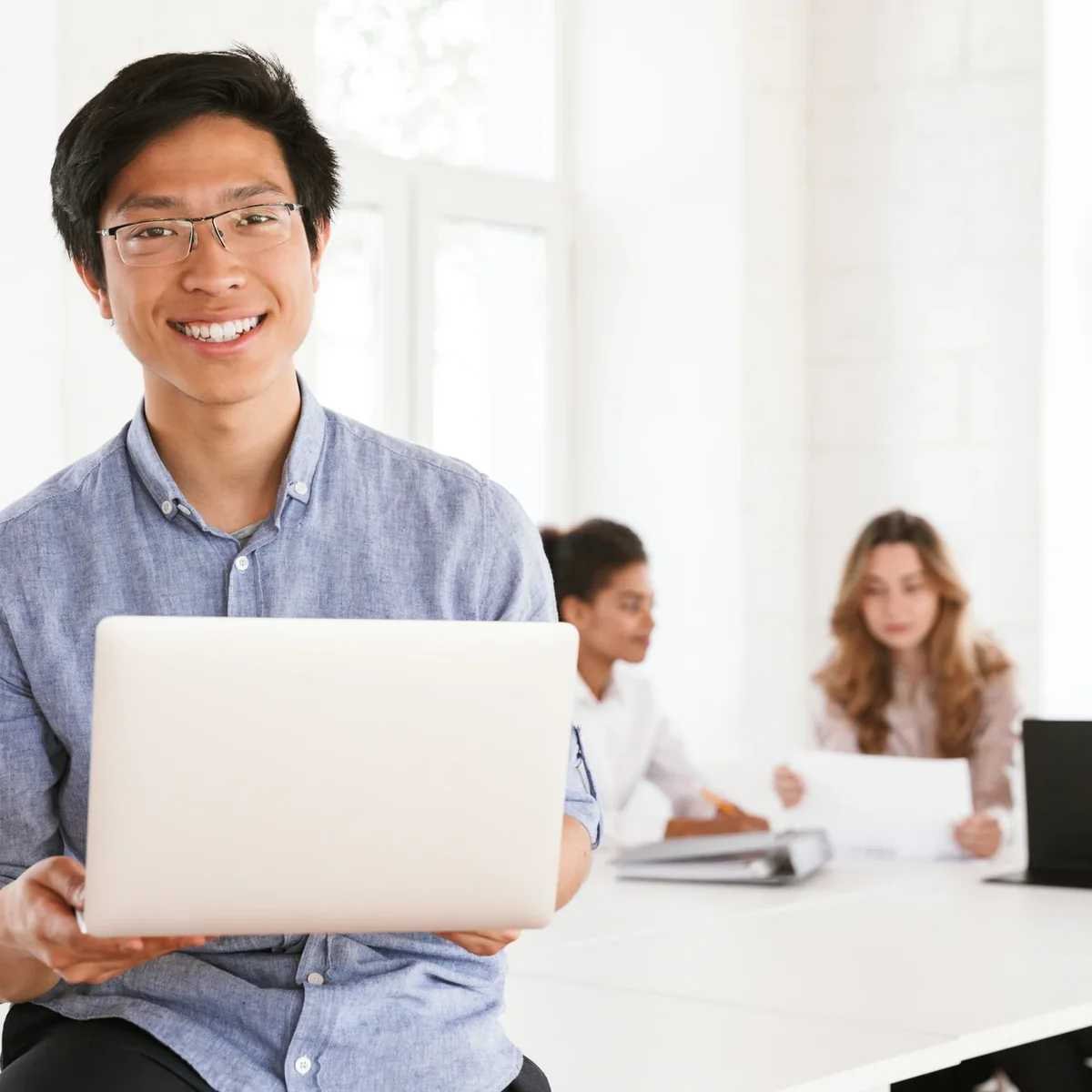 A professional holding a laptop in a shared workspace